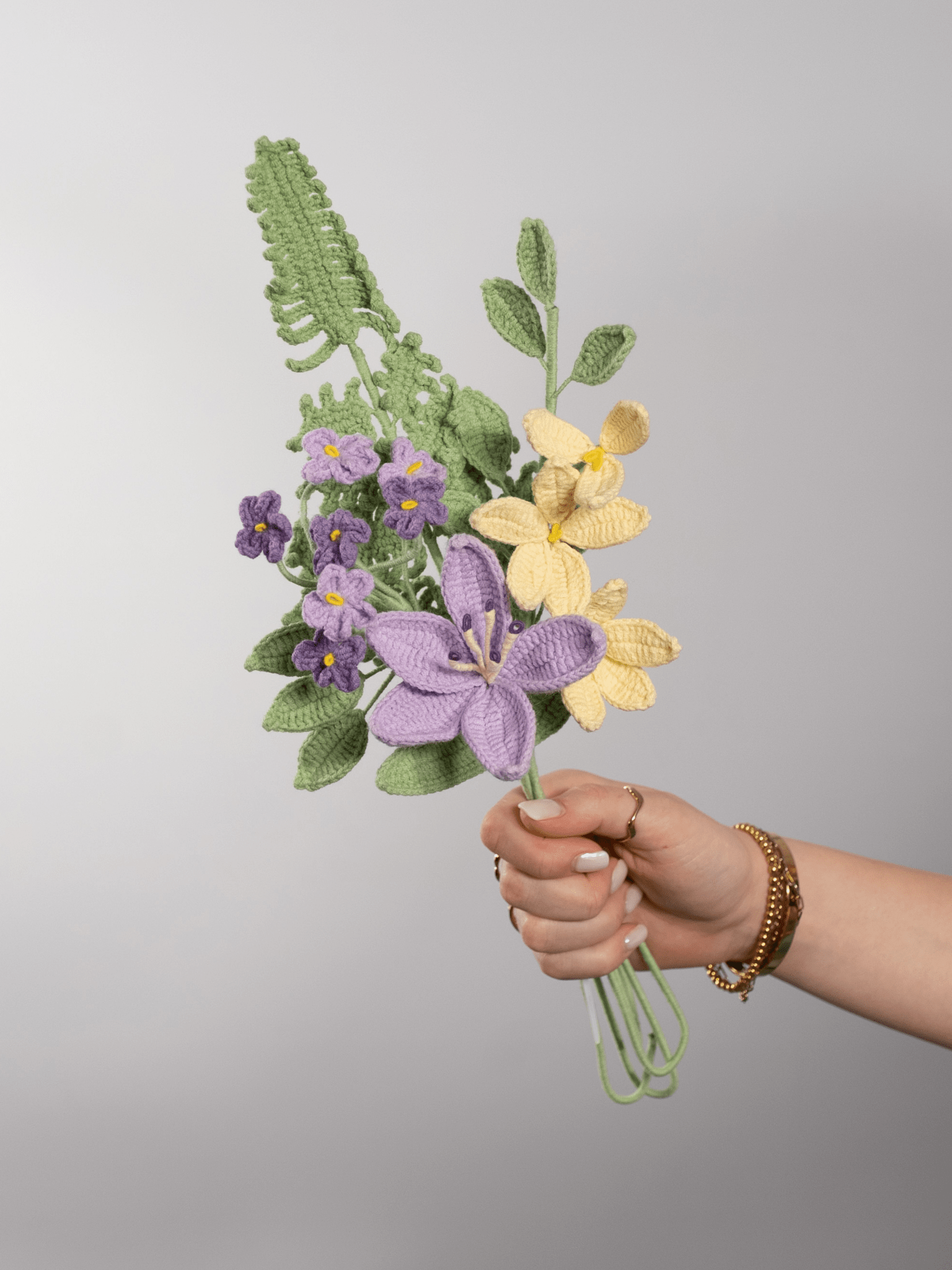 Der Blumenstrauß Lili Whisper wird in der Hand gehalten. Ein Produktbild des bloomly Strauß mit grauem Hintergrund